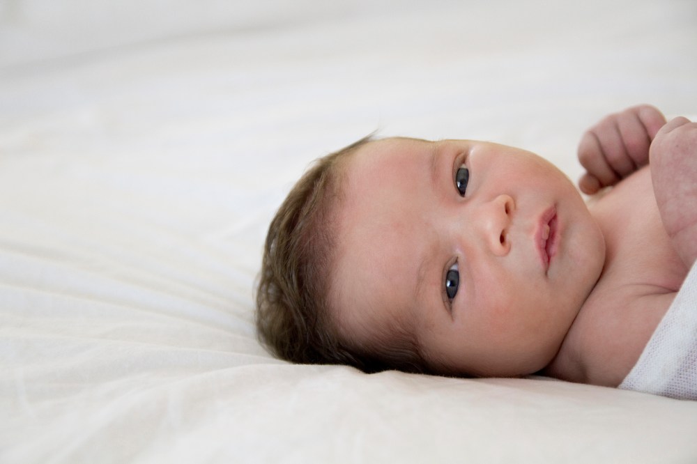 Awake baby, lying on white bedding making great eye contact.