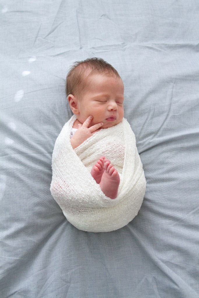 Newborn wrapped in white stretch fabric. Bundled up in a womb like pose. Photographed during a lifestyle newborn shoot.