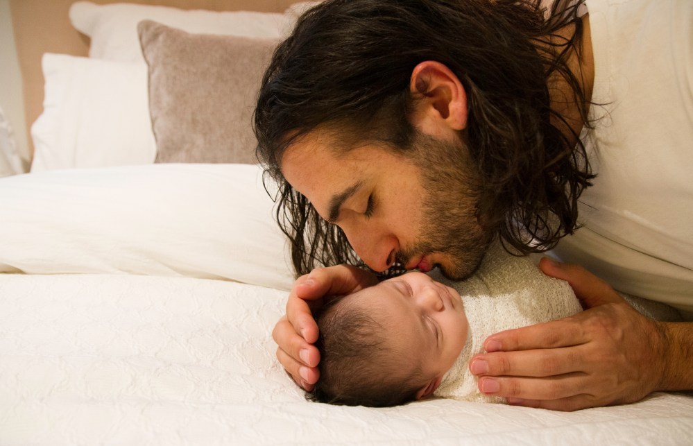 Father kissing newborn baby on cheek.