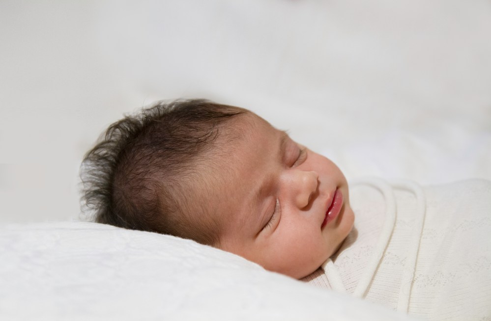 Sleeping newborn wrapped and photographed on white.