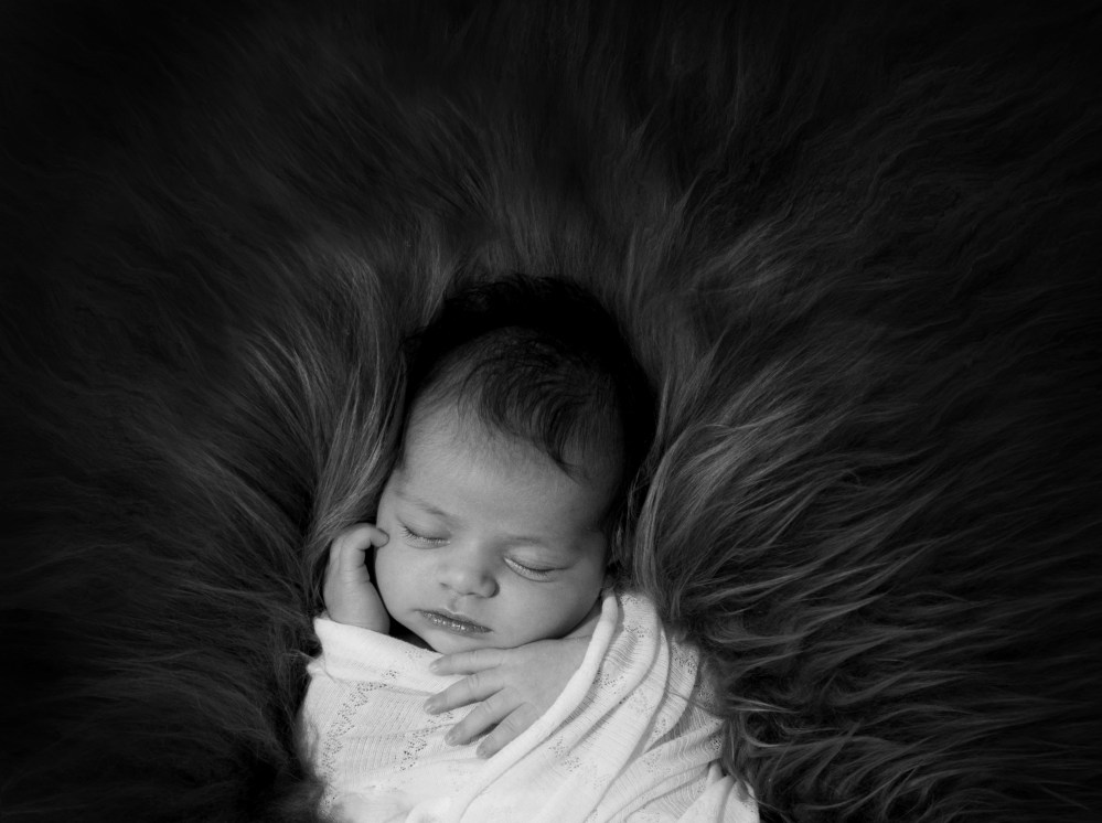 black and white newborn baby photograph. Baby asleep, wrapped lying on flokati fur.