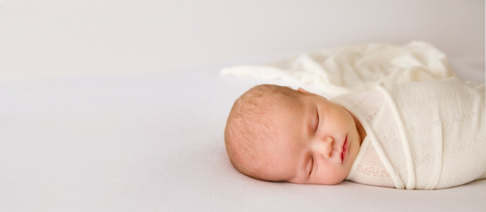 sleeping newborn wrapped in cream and white fabric. Wrap flowing behind baby. Studio photo shoot.