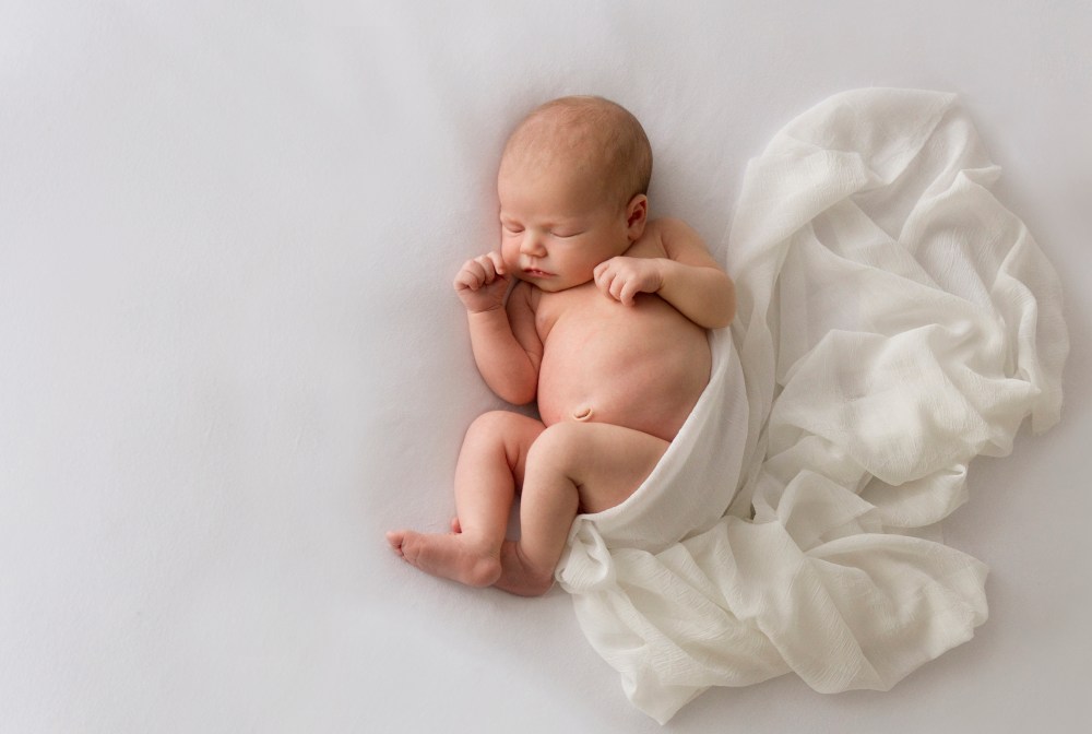 Newborn photography in studio. Baby photographed on beanbag, white wrap flowing out from behind baby.