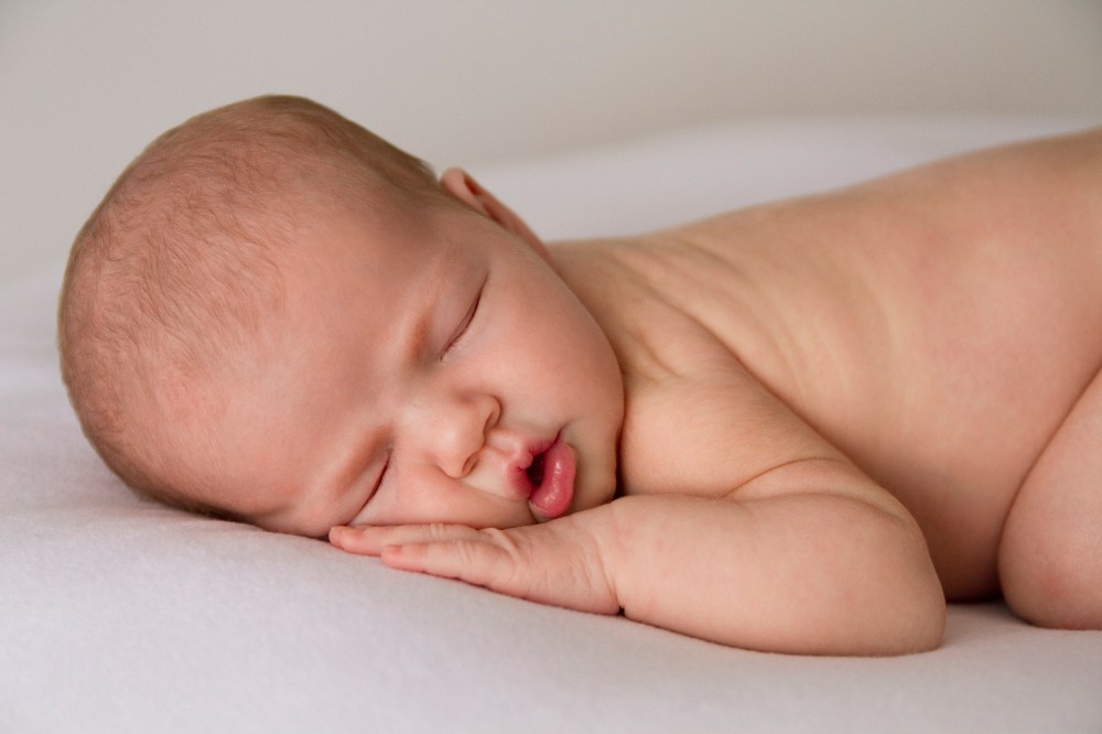 Close up photograph of newborn sleeping on tummy. Squishy baby cheeks and lips. Photographed in studio on white fabric.