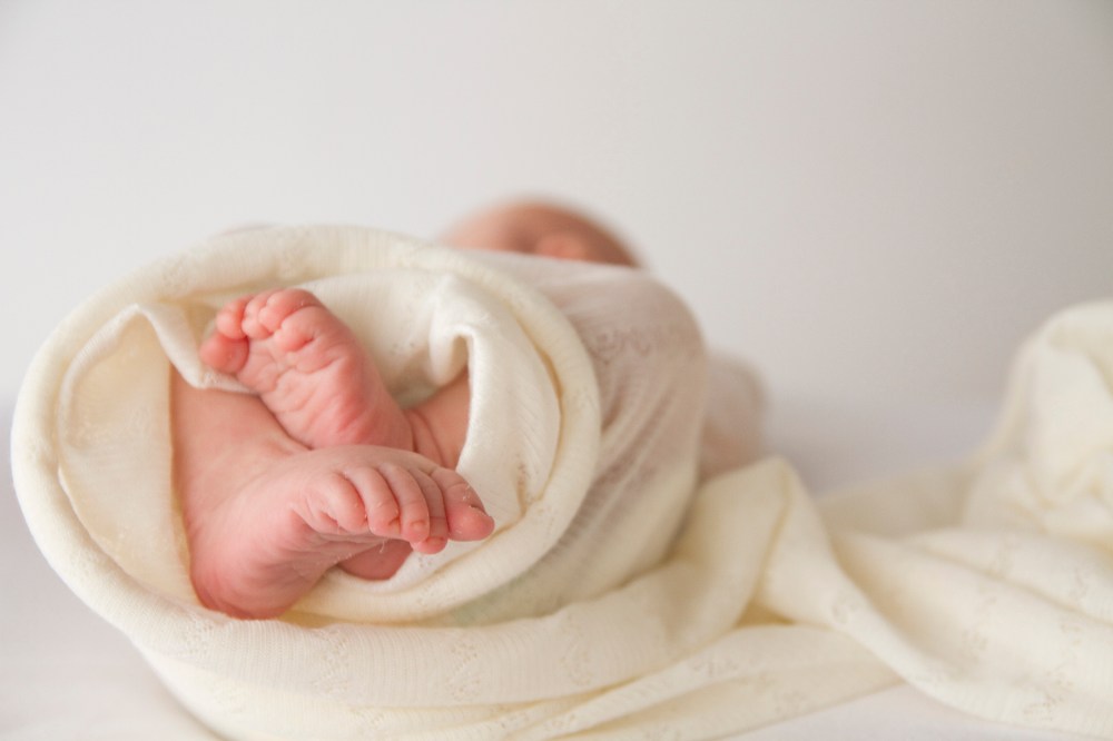 close up photo of newborn baby feet. baby wrapped in white stretch fabric.